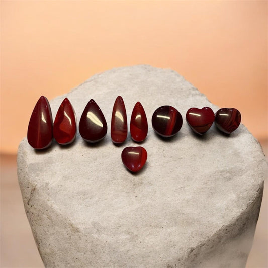 Collection of deep red Rosarita cabochons in pear, oval and heart shapes, handcrafted from rare gold slag material used in artisan jewellery making.
